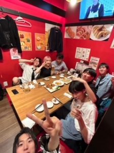 壁の色が赤い飲食店の個室に集う6人のゼミ生と宮本先生。