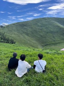 青空の下一面に広がる草原に座る3人の後ろ姿