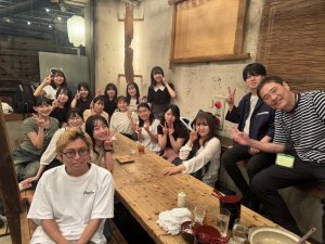 飲食店で机を囲んだ集合写真。中村先生と16人のゼミ生が笑顔でピースなどしている。