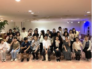 足立ゼミ集合写真その2。先生やゼミ生たちがポーズをとりかけているようで、ピースをしながら横を向いたり微笑んだりしている。