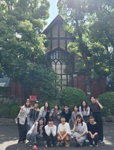 緑の木々に囲まれたレンガ造りの建物の前で、ポーズをとる海津ゼミの集合写真。