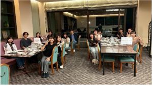 夕食会場の様子の写真。伊藤先生と13名が机いっぱいに広がったお皿を前に笑顔でピースしている。