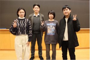 野村ゼミの集合写真。野村先生と学生3名が、黒板の前に立ってカメラに向かい、笑顔でピースサインをしている。