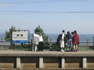 JR雨晴（あまはらし）駅のホームに立つゼミ生らしきグループ。ホームの向こうには青い海と空が広がり、景色の良い場所で記念撮影をしている様子。