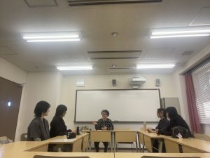 ロの字に机が並べられた教室で小林先生と4人のゼミ生がゼミをしている様子の写真