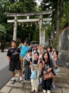 「諏訪大社」と書かれた柱と大きな鳥居を前に集まる10人のゼミ生の写真。みんな笑顔でピースなどをして明るい表情をしている。