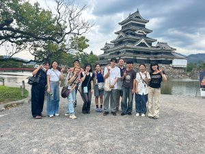 松本城を背景にピースして撮られた佐藤先生と10人のゼミ生たちの集合写真。