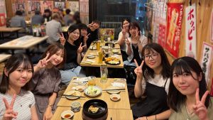 水戸ゼミ3年生の懇親会または打ち上げの写真。居酒屋でテーブルを囲み、全員がピースサインをして楽しんでいる。